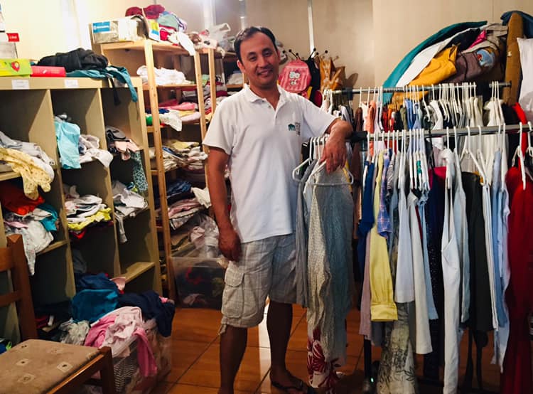 a man stands next to rails of clothes in the CRIBs Free Shop